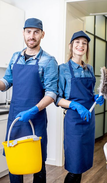 Portrait of a couple as a professional cleaners in uniform standing together with cleaning tools indoors